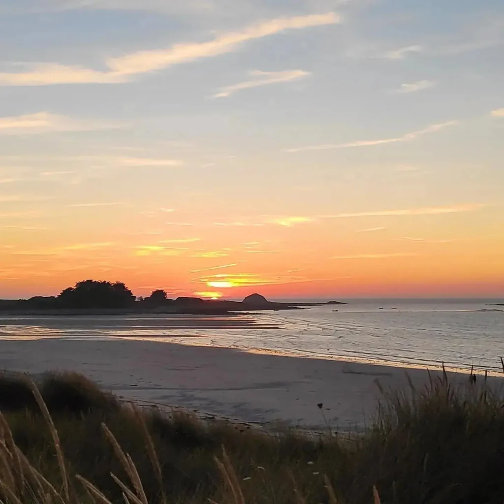 Plage portsall couchée de soleil Cette image capture un coucher de soleil sur une plage à Portsall, teintant le ciel de jaune à violet. Le sable de la plage est parsemé de flaques qui reflètent la lumière du soleil couchant. Des îlots rocheux émergent de l'eau calme à l'horizon, et des herbes hautes bordent la plage. Au loin, on pourrait imaginer une maison de location à Portsall, offrant une vue imprenable sur cette scène paisible.